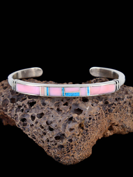 Silver bracelet with pink and blue inlay on a dark rock background
